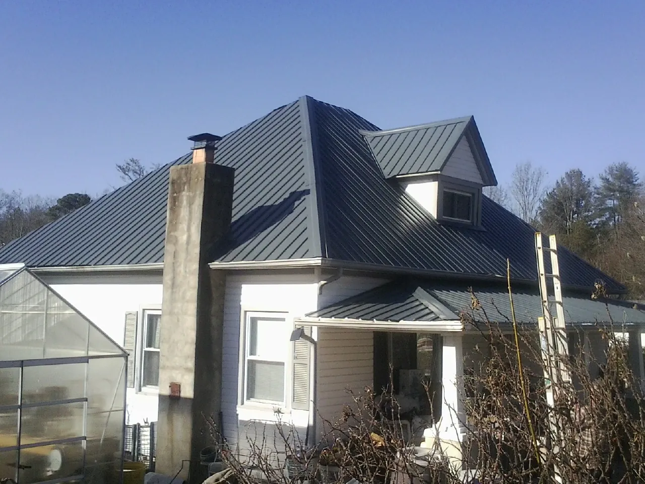 Dark blue standing seam metal roof on a white farmhouse with dormer — Slate & Tile Roof Repair by Roofing Brothers in Cambridge